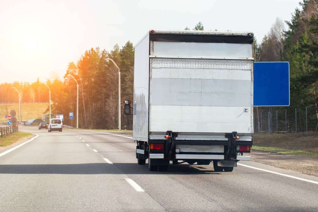 A commercial van with a tail lift driving along a road.